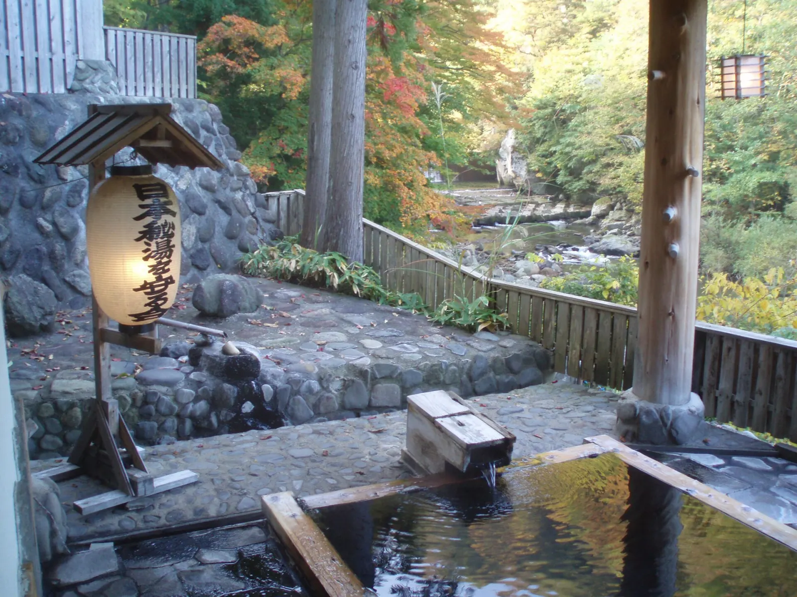An open-air stone bath beside a river, autumn trees around it