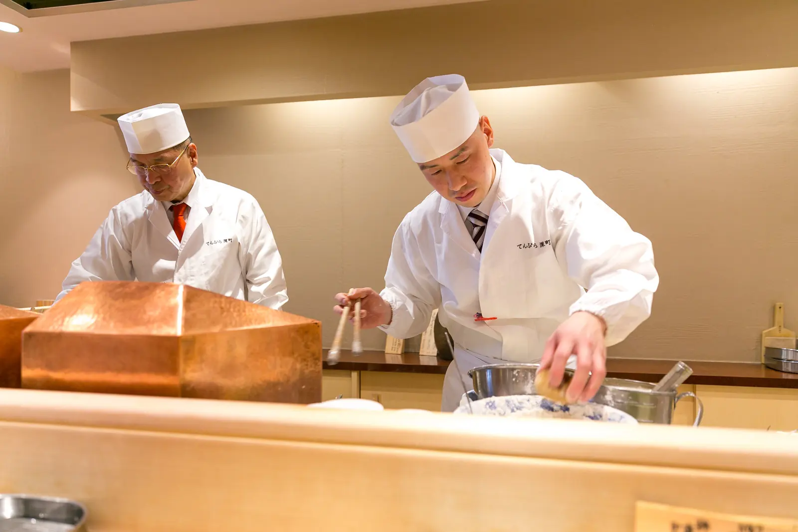 Two tempura chefs at the counter, the copper pot between them