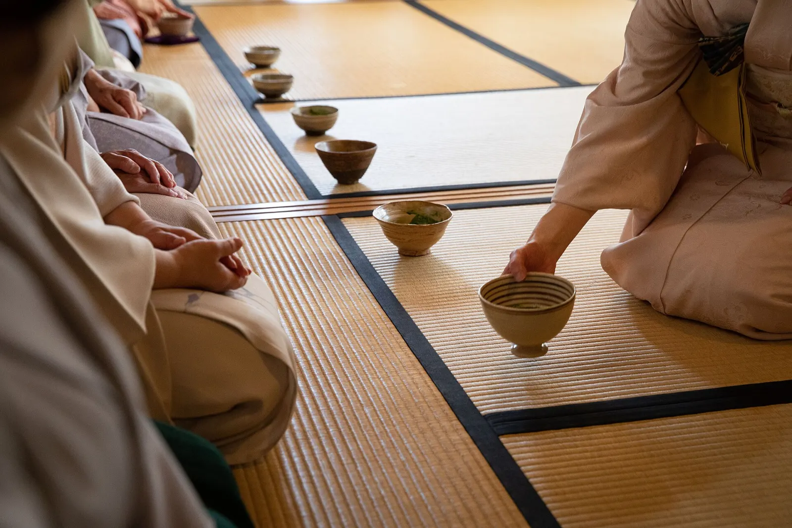 A host setting out tea bowls on tatami for guests