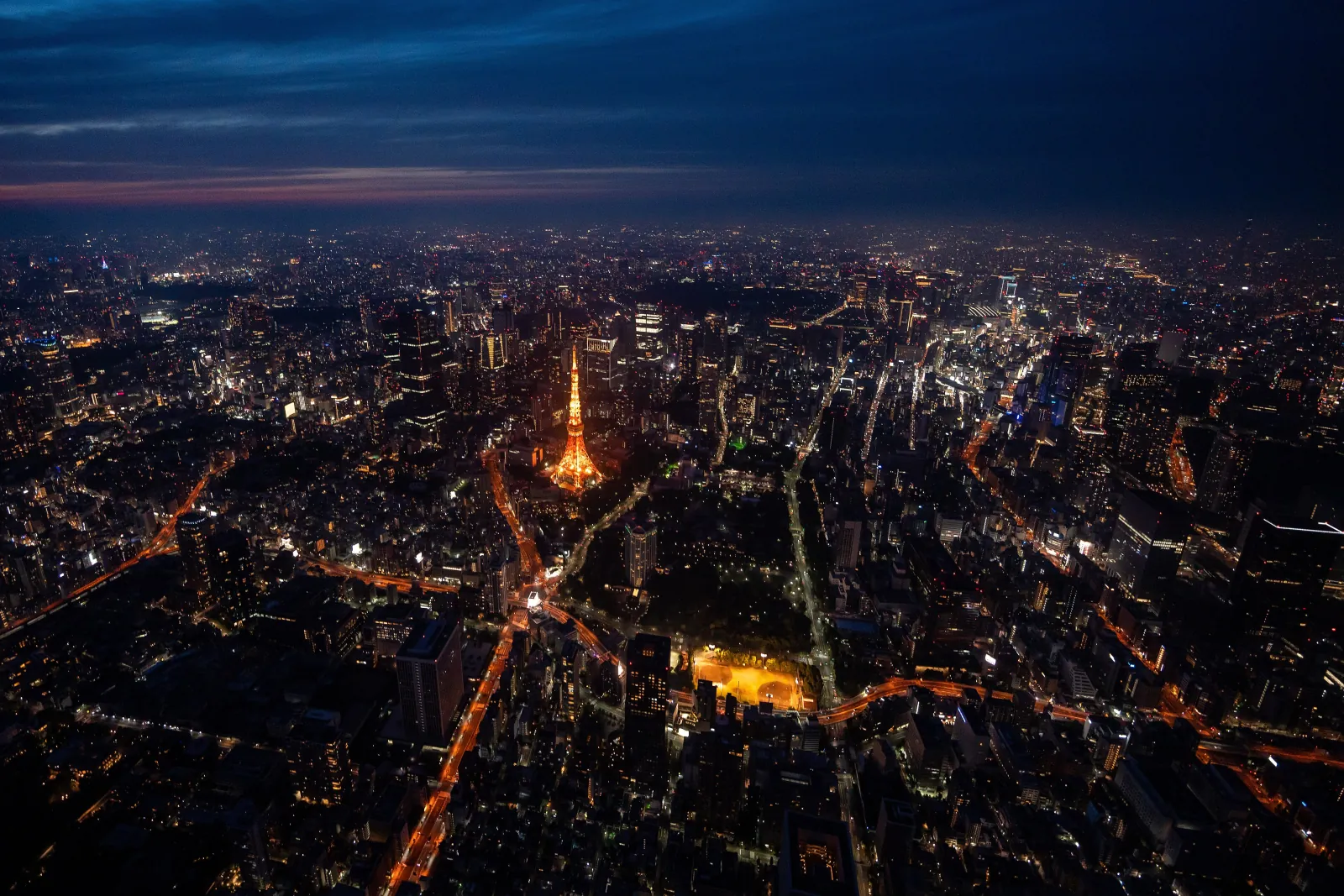 Tokyo Tower glowing below at dusk, seen from the air