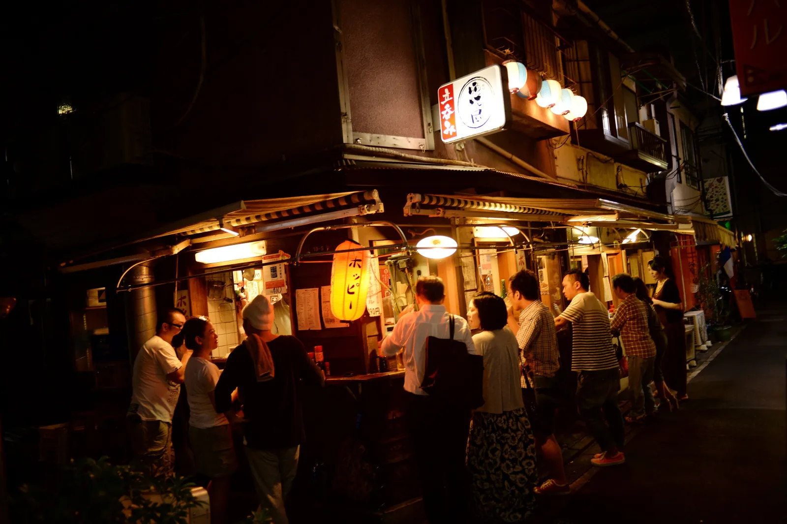 Regulars standing at a lantern-lit bar on a Tokyo side street
