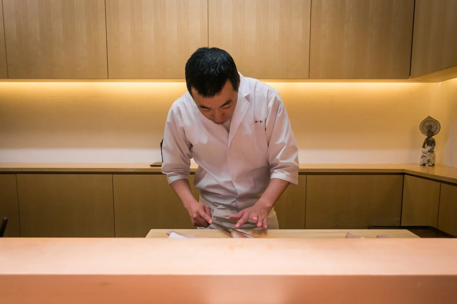 A sushi chef at work behind a pale hinoki counter