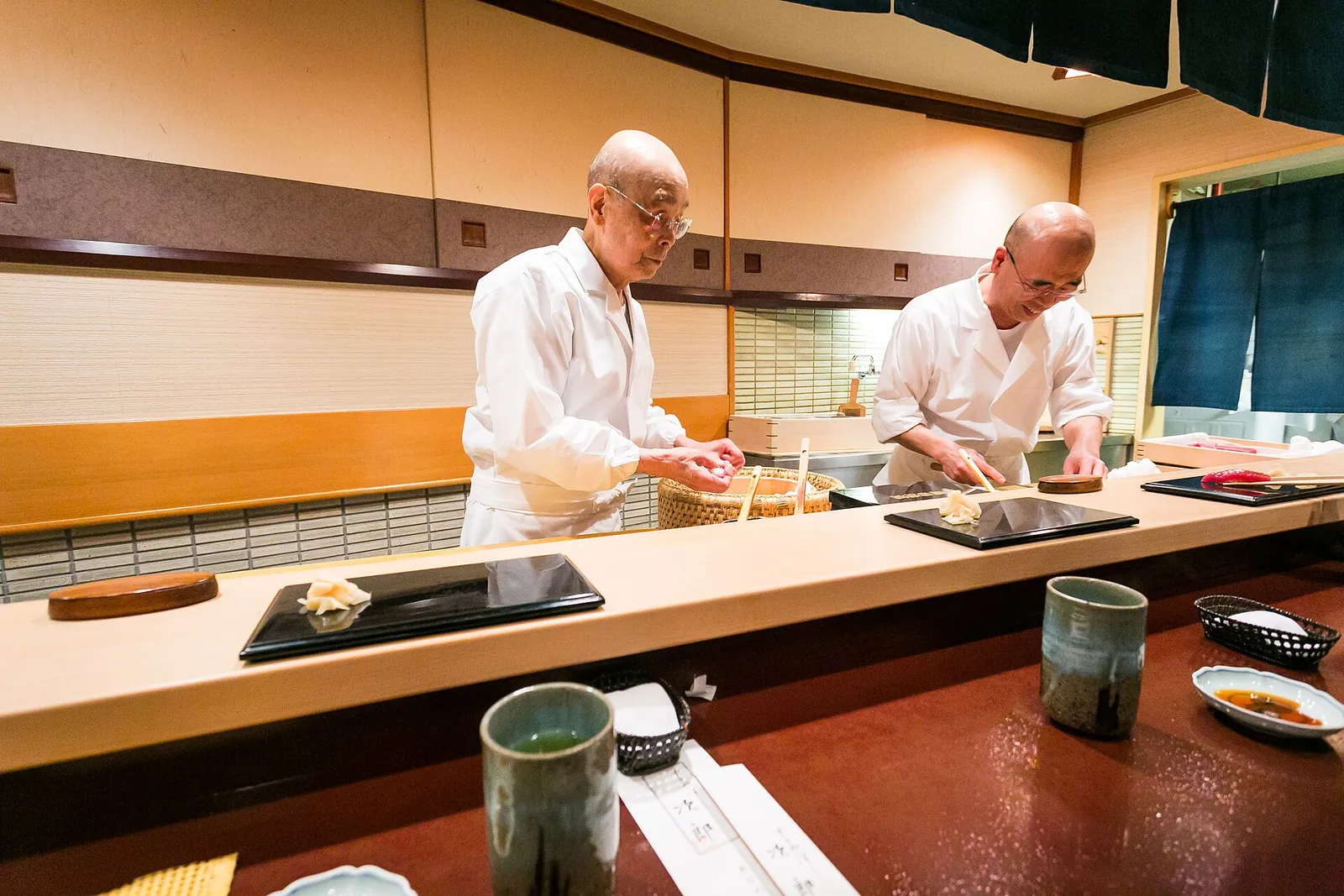 Two sushi chefs at work behind a pale counter